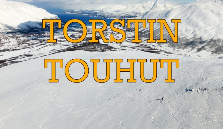Kansikuva Torstin Touhut -kanavalle. Panoraamakuva lumisesta Lyngen-vuoristosta Norjassa. Kuvan etualalla avara laskettelurinne ja kaksi pientä vapaalaskijaa. Taustalla näkyy vuono ja vuoria. Keskellä kuvaa oranssilla tekstillä Torstin Touhut